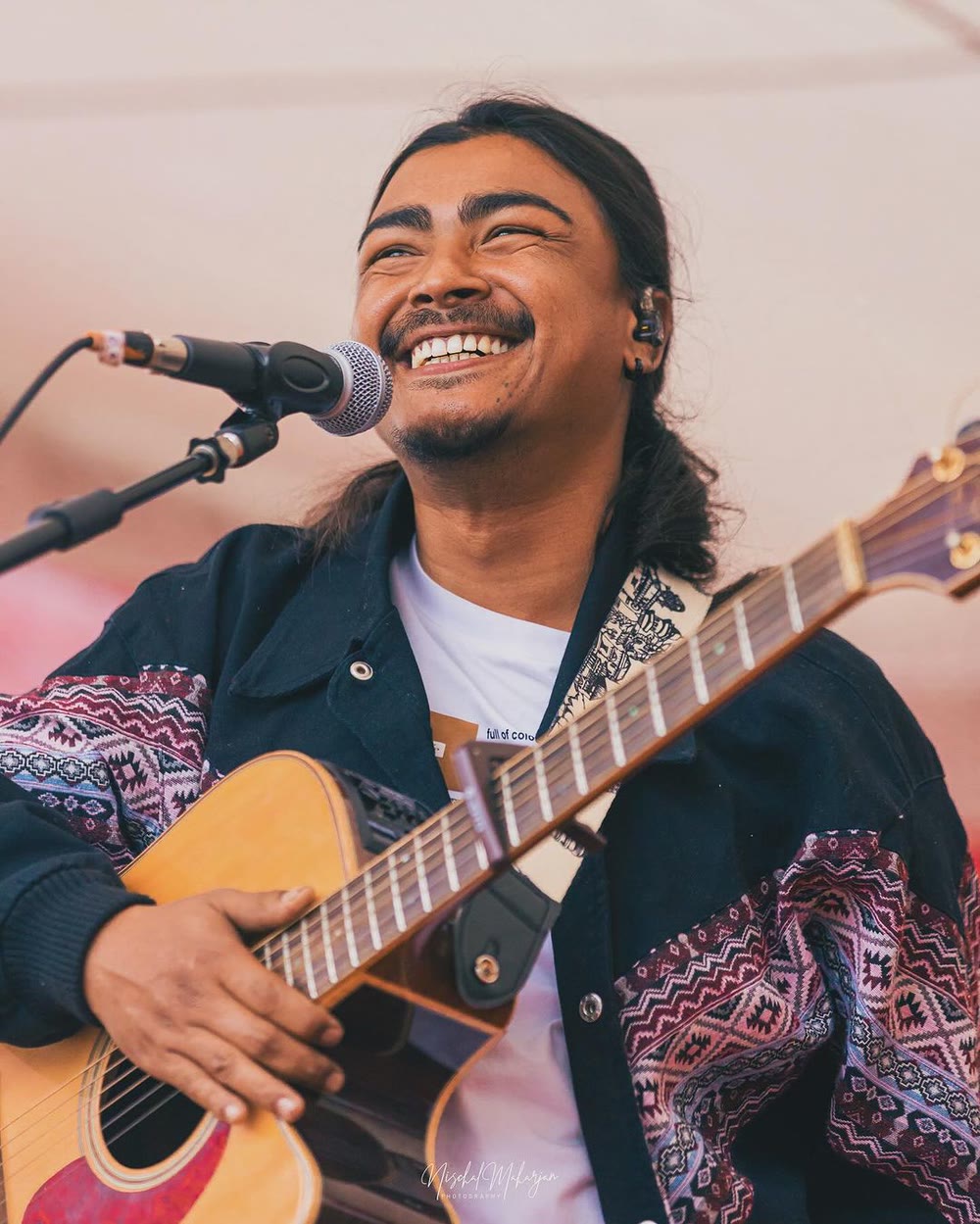 Kuma Sagar smiling mid-performance with an acoustic guitar
