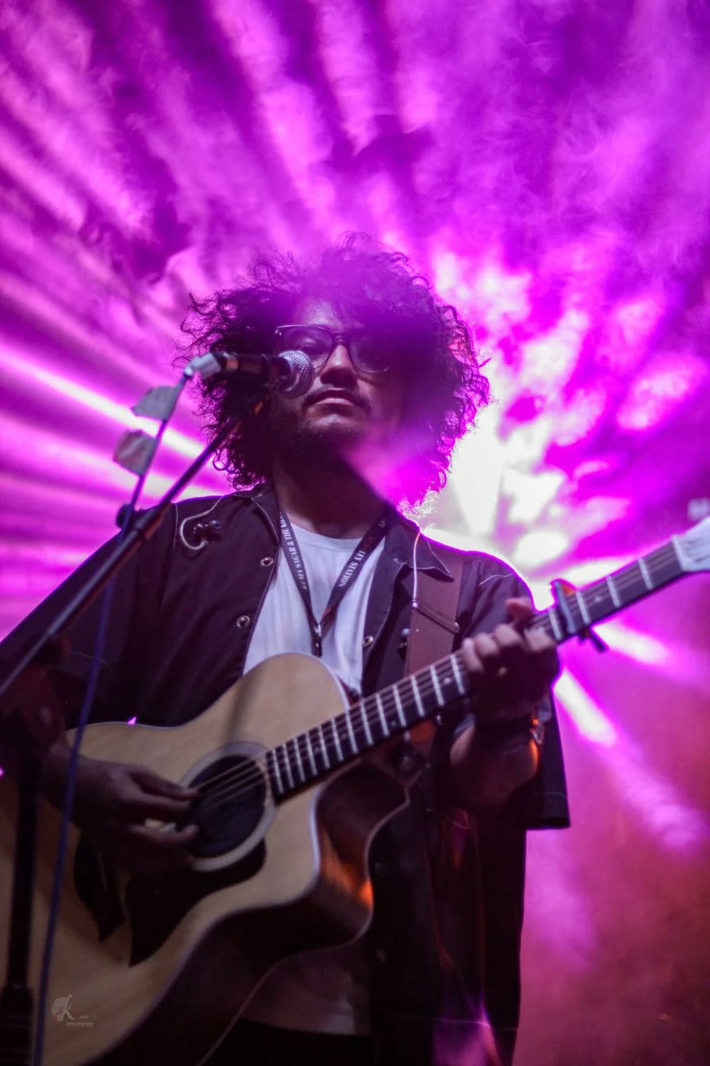 Kuma Sagar performing with an acoustic guitar in magenta stage light